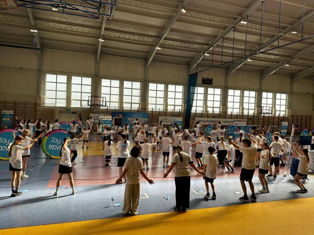 Uczniowie ćwiczą razem na hali sportowej podczas zajęć ruchowych.
