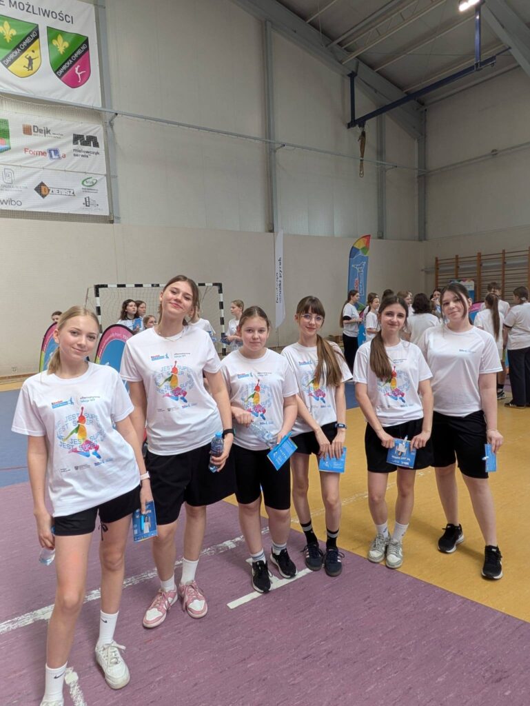 Grupa uczennic w strojach sportowych w hali podczas wydarzenia „Joy of moving”.