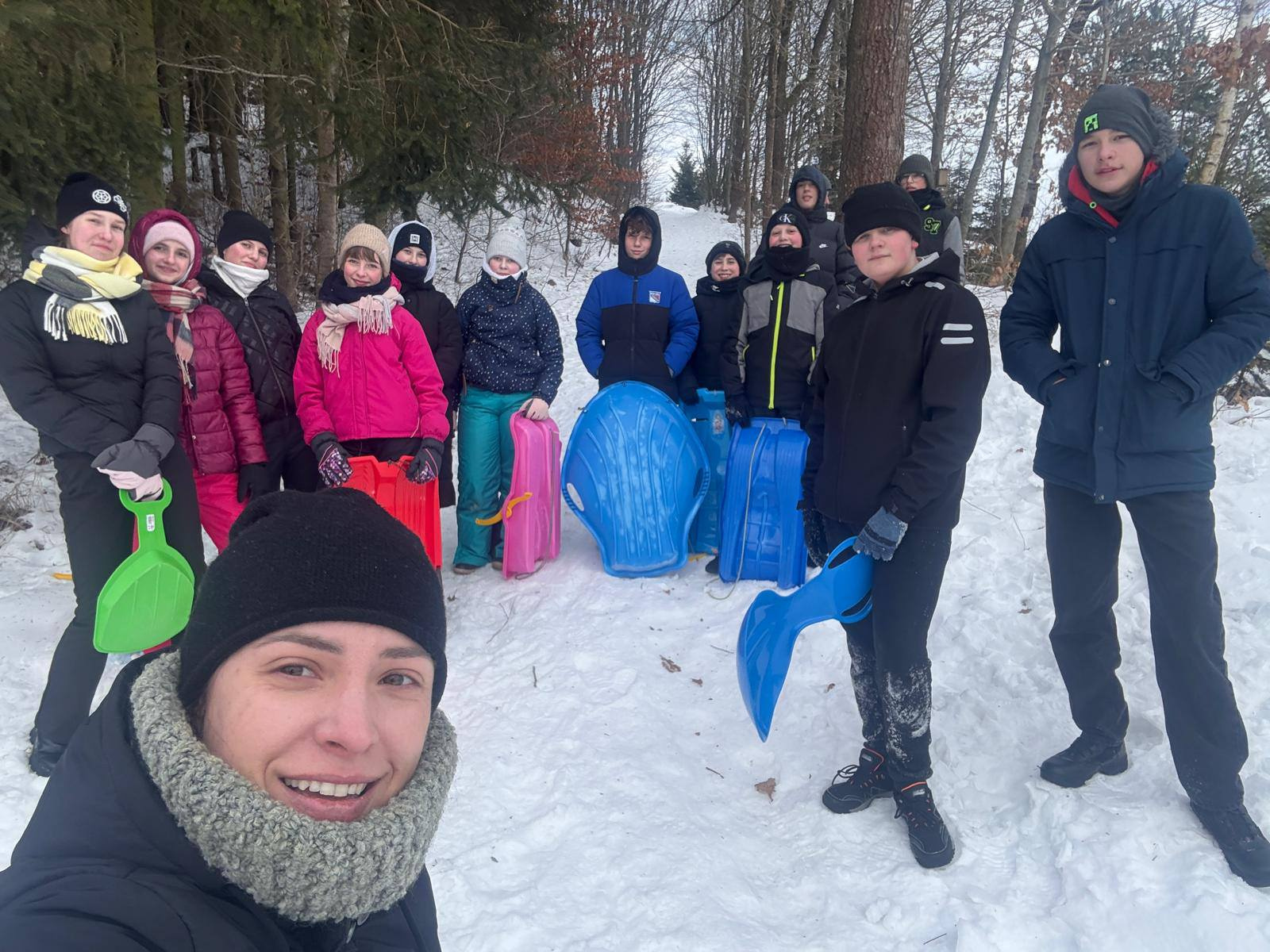 Uśmiechnięta nauczycielka robi selfie z uczniami podczas zimowego kuligu na świeżym powietrzu.