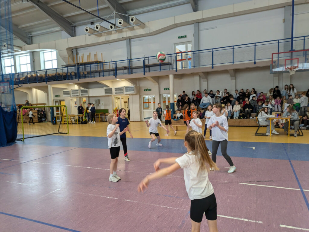 Uczennice grają w piłkę siatkową na sali gimnastycznej podczas szkolnych zawodów sportowych.
