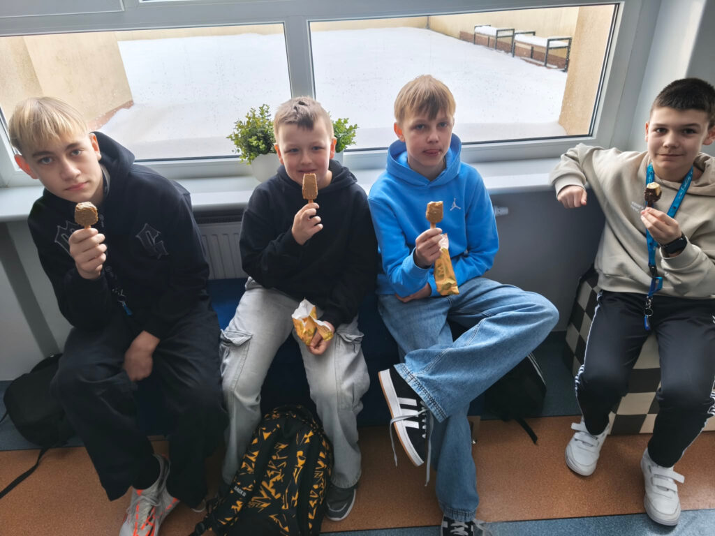Czterech uczni贸w siedzi na korytarzu i je lody podczas przerwy.