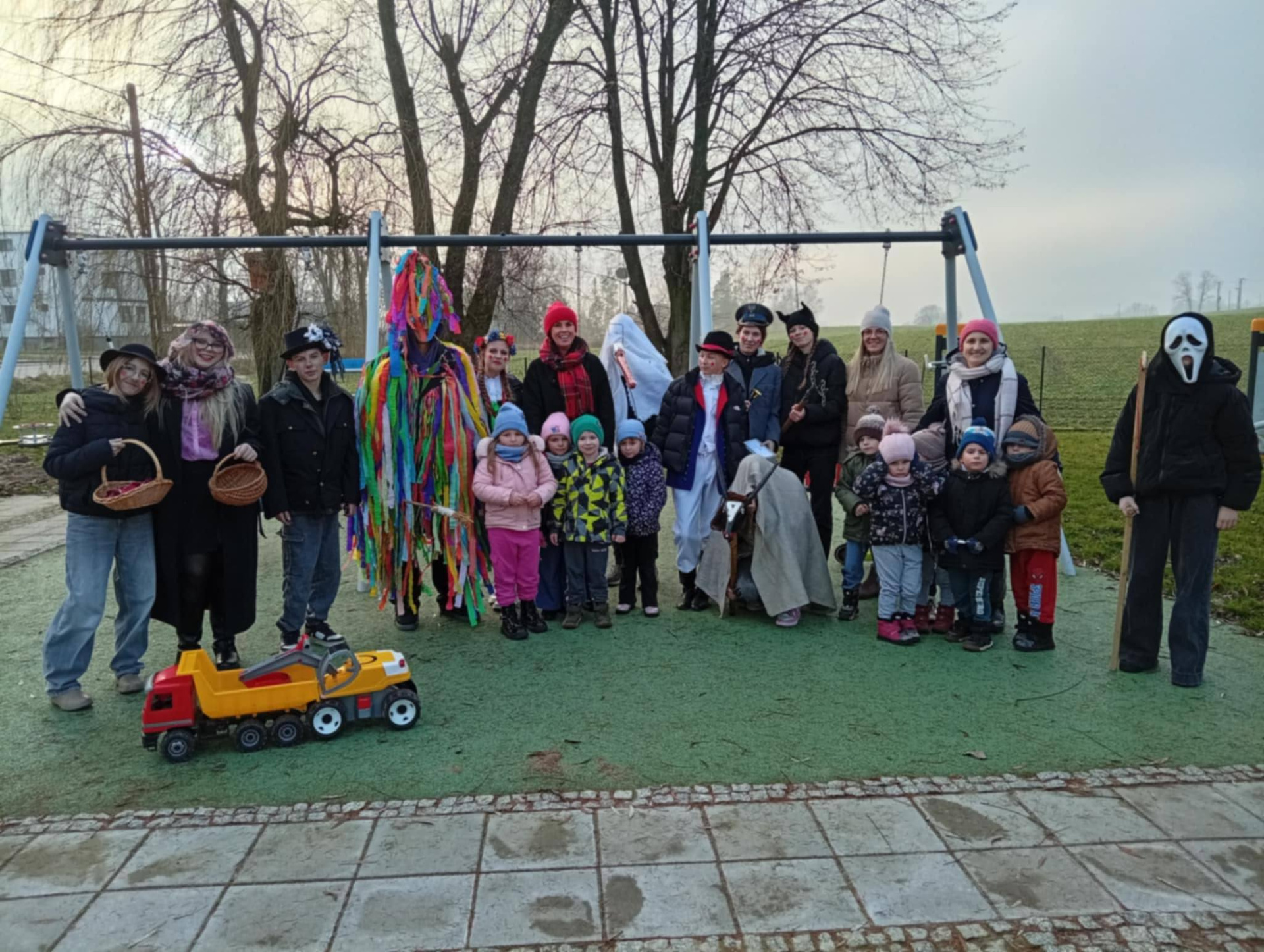 Wspólne zdjęcie kolędników z grupą młodszych dzieci na zewnątrz szkoły.