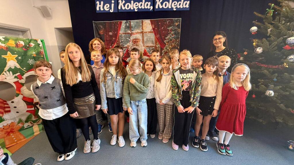 Grupa starszych uczniów z nauczycielkami przed świąteczną dekoracją i ubraną choinką.