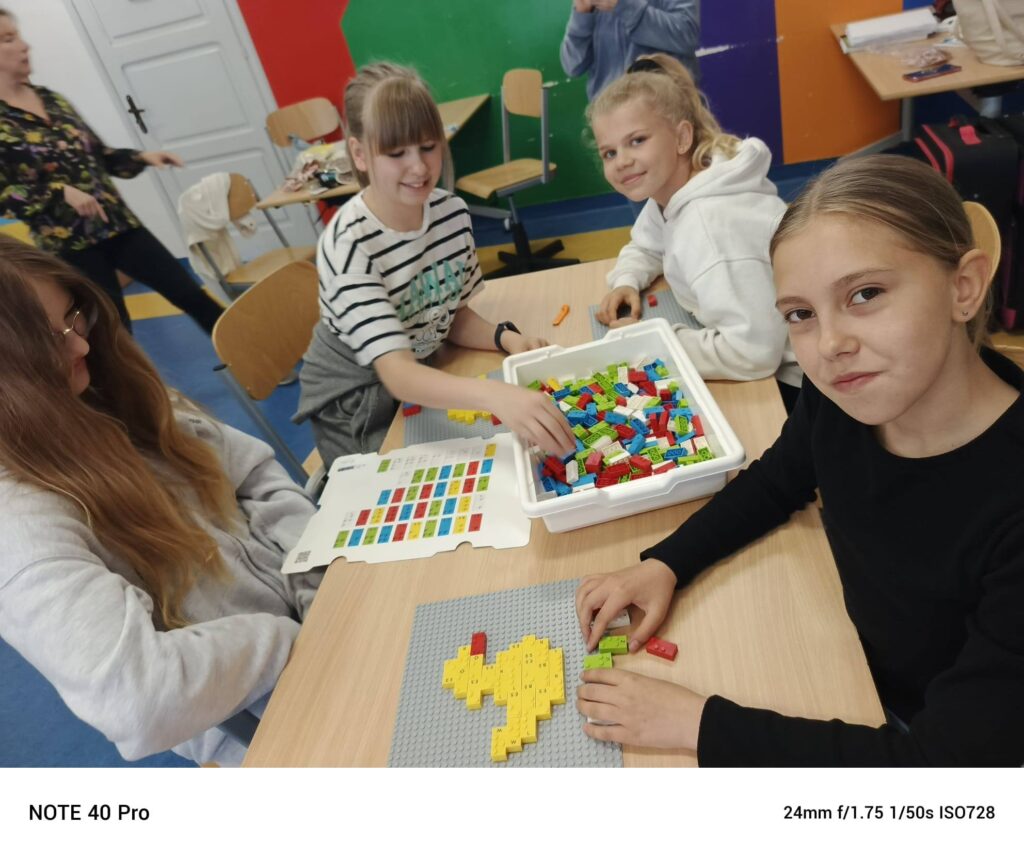 Uczniowie siedzący przy stoliku i układający wzory z kolorowych klocków na szarych podkładkach.
