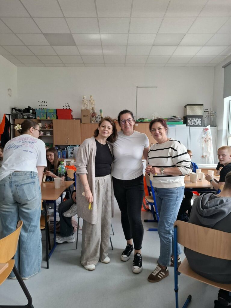Trzy nauczycielki pozują do zdjęcia w pracowni szkolnej podczas spotkania integracyjnego uczniów i kadry pedagogicznej.