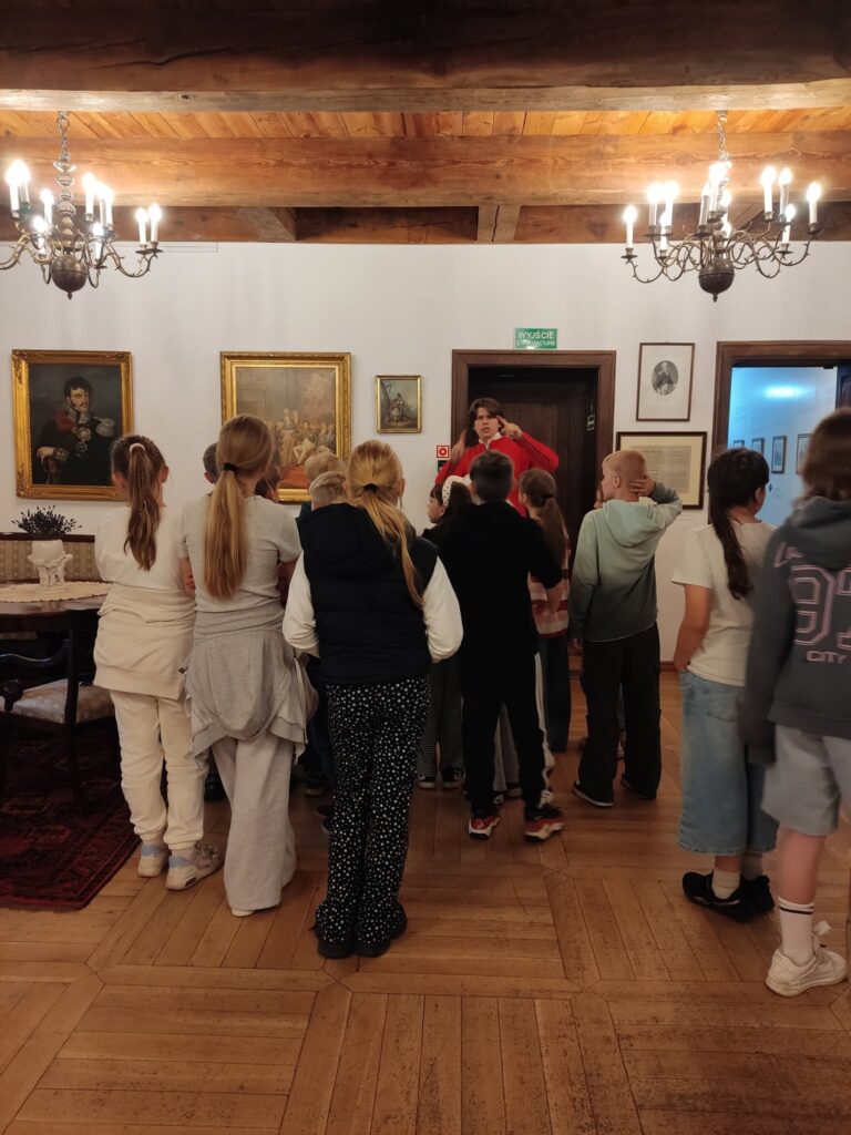 Uczniowie podczas zwiedzania zabytkowych wn臋trz muzeum s艂uchaj膮 opowie艣ci przewodnika o historii dawnego dworu.