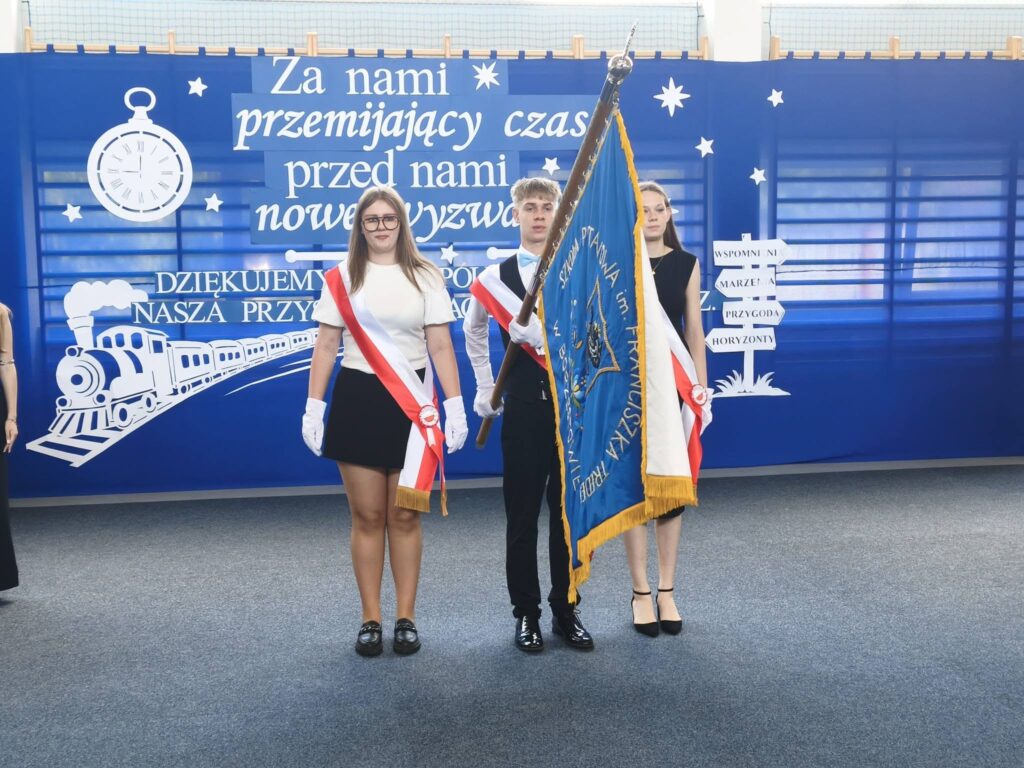 Poczet sztandarowy szkoły uczestniczy w uroczystym zakończeniu roku szkolnego. Na tle okolicznościowej dekoracji uczniowie pełnią honorową wartę, podkreślając podniosły charakter wydarzenia.