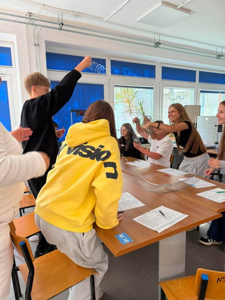 Uczniowie podczas zajęć wykonują doświadczenie z wykorzystaniem sprężyny i innych materiałów edukacyjnych.